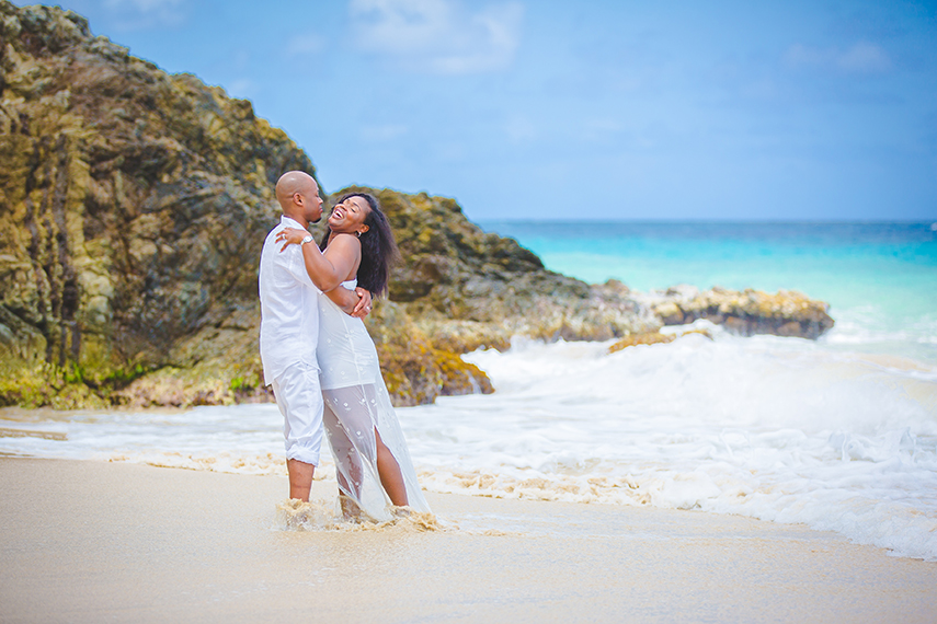 black bride and groom hugging on St Croix beach with bright blue Caribbean ocean in the background