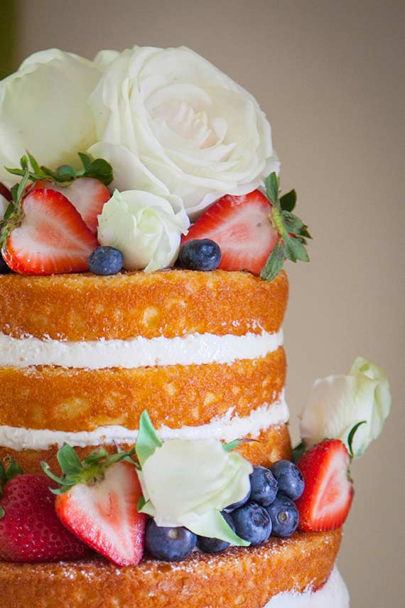 naked cake with white roses strawberries and blueberries and white icing
